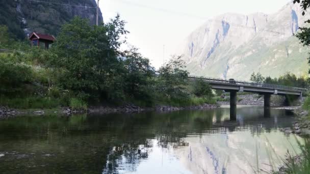 4Kシネマティック映像 川に架かる小さな橋を眺めます 車が通り過ぎている 背景に山を持つノルウェーの風景 — ストック動画