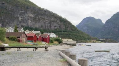 Kıyıda kırmızı evler (rorbas) ile fiyort tipik Norveç görünümü. Suda yüzen küçük balıkçı tekneleri.