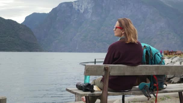 年轻的女旅行者坐在长凳上 看峡湾和休息 大背包站在她旁边 — 图库视频影像