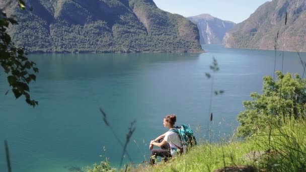 Mujer joven con una gran mochila sentada al borde de la colina — Vídeos de Stock