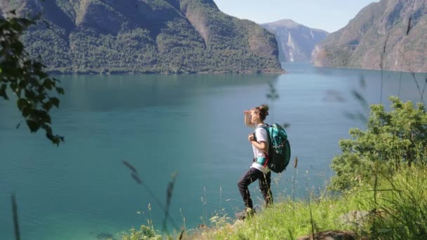 Ung kvinne med en stor ryggsekk som står på kanten av åsen – stockvideo