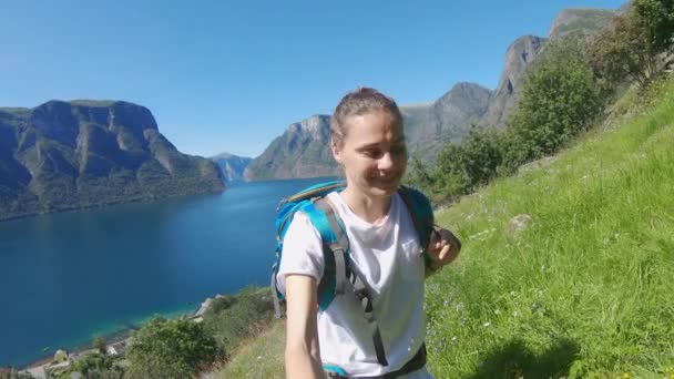 Fiatal nő hátizsákos csinál egy szelfit a háttér egy norvég fjord — Stock videók