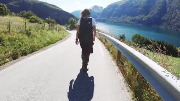 Счастливая молодая женщина-бэкпекер, идущая по горной дороге с видом — стоковое видео