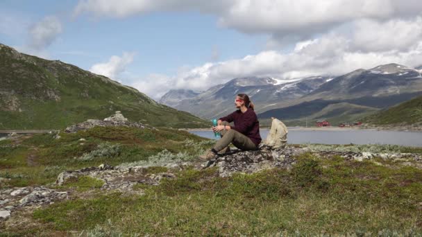 Ung kvinna resenär sitter på klippan och dricker vatten från flaskan — Stockvideo