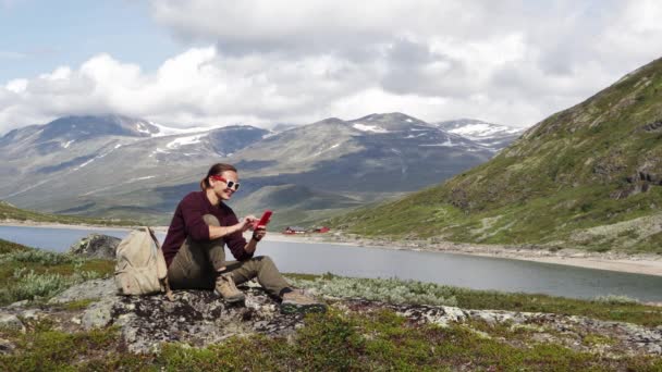 Mladá žena cestovatel relaxaci na vrcholu kopce a pomocí svého smartphonu. — Stock video