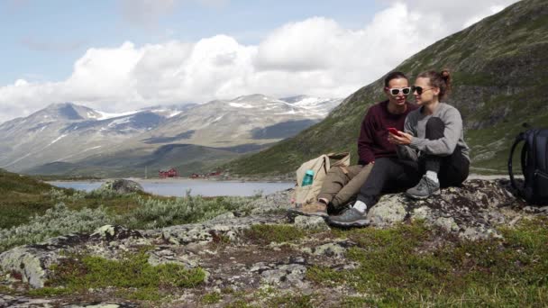 Twee jonge vrouwelijke reizigers die een smartphone gebruiken met het oog op een Noors fjord — Stockvideo