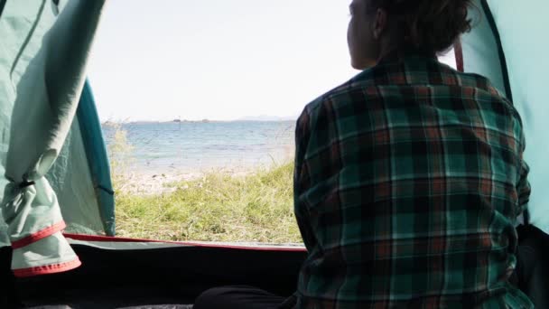 En ung kvinnlig resenär sitter inne i sitt turisttält. — Stockvideo