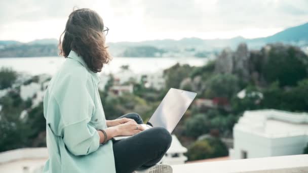 Joven estudiante disfrutando de una vista superior de la ciudad mientras usa su computadora portátil — Vídeos de Stock