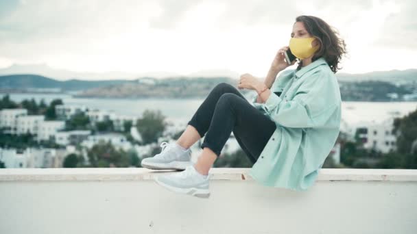 Una joven con una máscara de color amarillo brillante habla por teléfono — Vídeo de stock