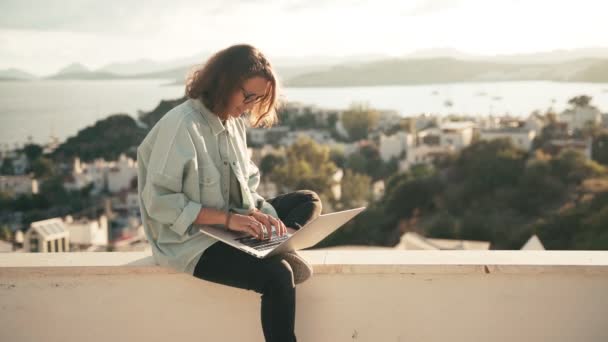 Молодая студентка наслаждается видом на город, пользуясь ноутбуком — стоковое видео