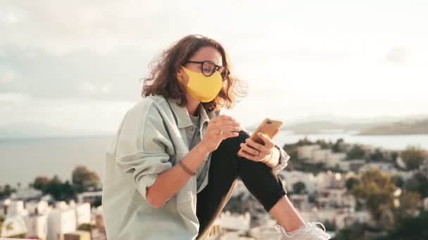 Uma jovem mulher com máscara protetora desbloqueia seu smartphone com um id facial — Vídeo de Stock