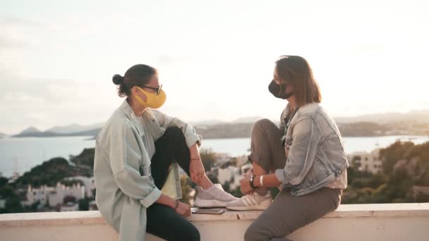 Twee jonge vrouwen in heldere beschermende gezichtsmaskers praten — Stockvideo