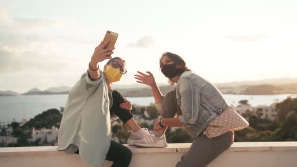 Twee jonge vrouwen in beschermende gezichtsmaskers nemen van een selfie met een smartphone — Stockvideo