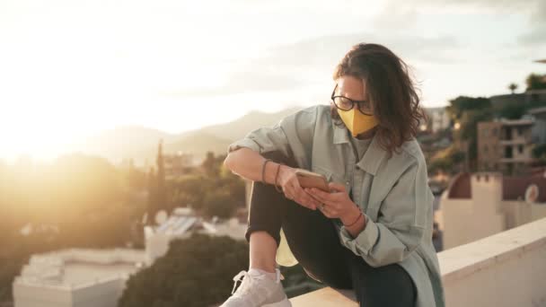 Mujer joven en gafas y una máscara protectora de color amarillo brillante usando su teléfono inteligente — Vídeos de Stock