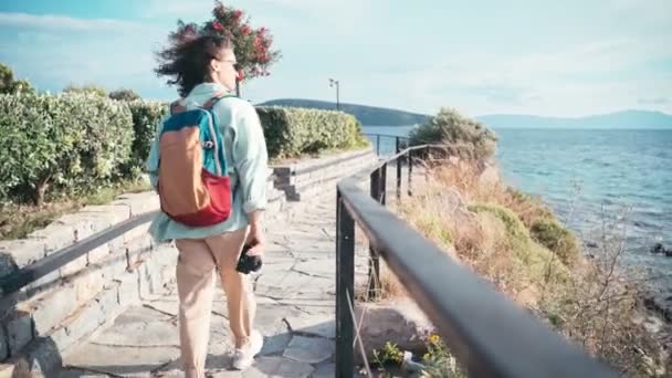 Uma jovem caminha ao longo do mar em um dia ventoso, com câmera fotográfica nas mãos — Vídeo de Stock