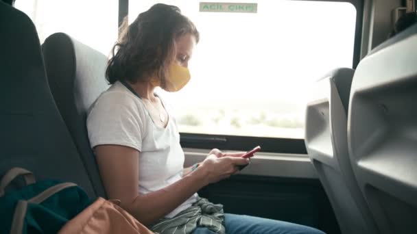 Молодая женщина в защитной маске в автобусе общественного транспорта со смартфоном — стоковое видео