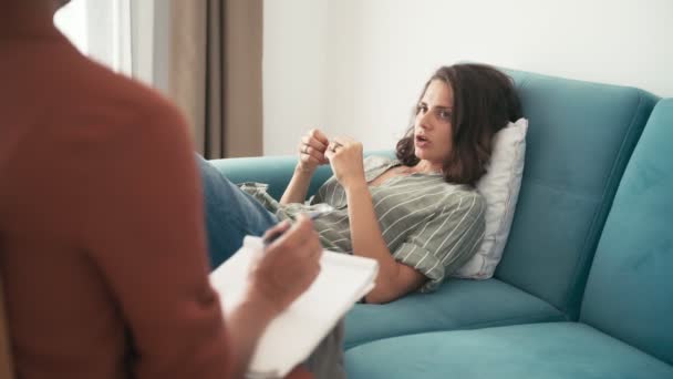 Mulher deprimida deitada no sofá durante a psicoterapia, psicóloga fazendo anotações — Vídeo de Stock