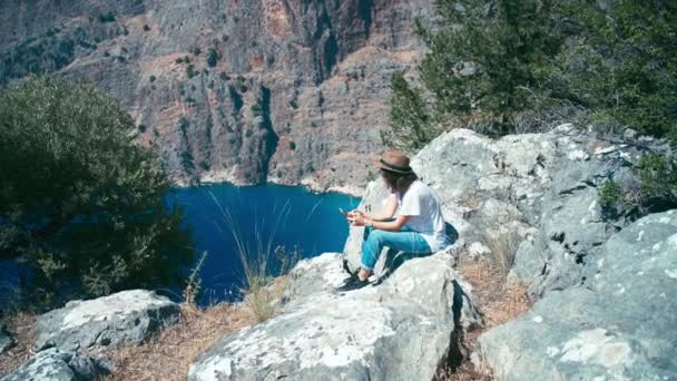 Молода жінка відеоблог, сидячи на краю скелі — стокове відео