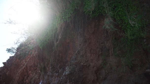 Blick von unten auf einen schönen kleinen Wasserfall auf dem Felsen mit gleißendem Sonnenlicht. — Stockvideo