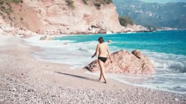 Bikinili genç bir kadın boş kumsalda yürüyor.