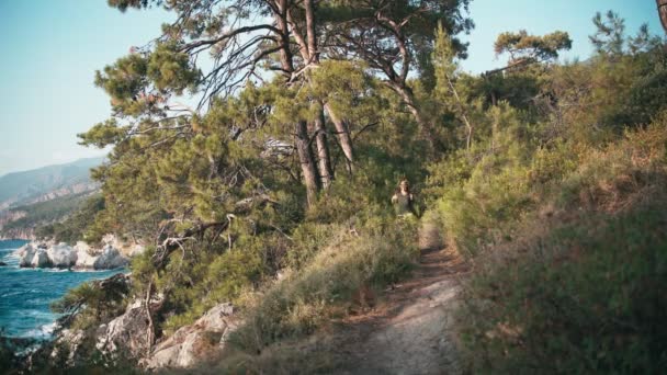Een jonge vrouw wandelend in het bos met uitzicht op zee langs de wandelweg — Stockvideo