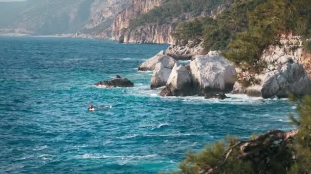 Dalgalı açık mavi deniz manzarası ve çam ağaçlarıyla kayalık deniz manzarası. — Stok video