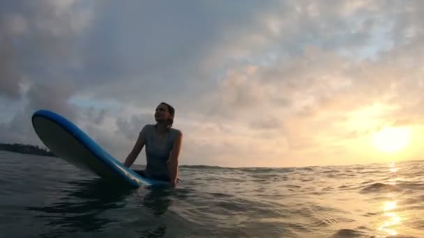 Une jeune femme est assise sur une planche de surf douce dans l'océan et attend une vague — Video