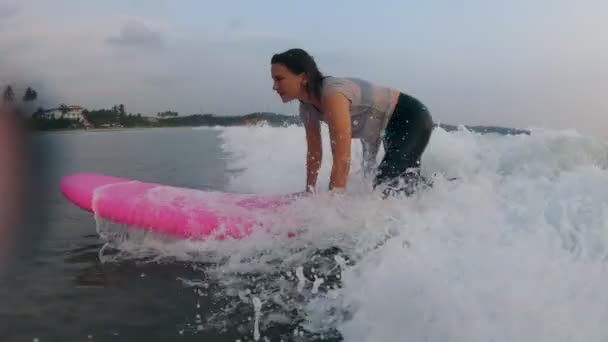 Uma jovem mulher de fato de banho aprende a surfar numa prancha de surf suave — Vídeo de Stock