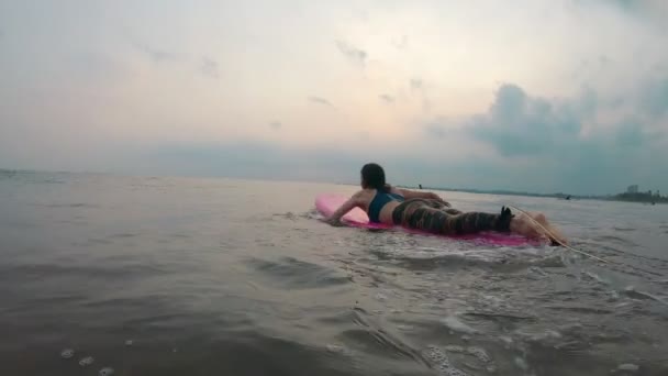 Молода жінка лежить на м'якій дошці для серфінгу і веде до океанічної хвилі — стокове відео