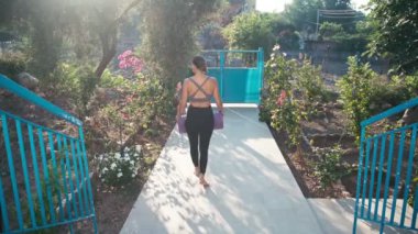 Yoga minderli genç bir kadın sabah sporu için kır evinden çıkıyor.