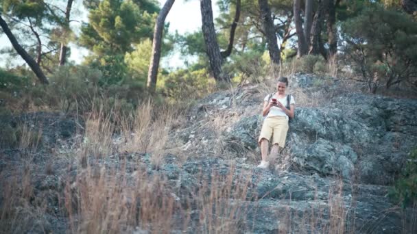 Mujer joven de pie en una ladera rocosa de la montaña usando su teléfono inteligente — Vídeo de stock