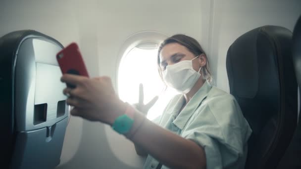 Junge Frau mit Gesichtsschutzmaske macht Selfie an Bord eines Flugzeugs — Stockvideo