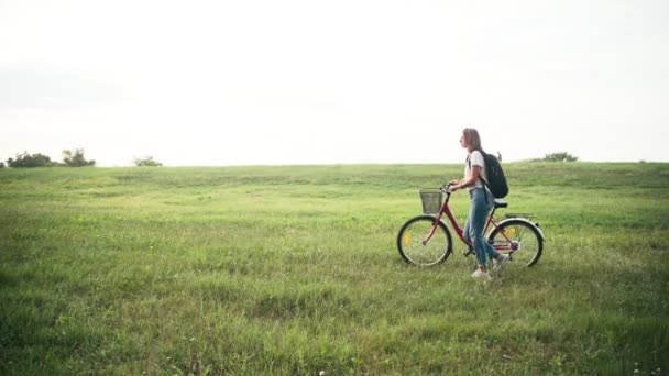 Yeşil bir alanda bisikletiyle yürüyen genç bir kadının sinematik görüntüleri. — Stok video