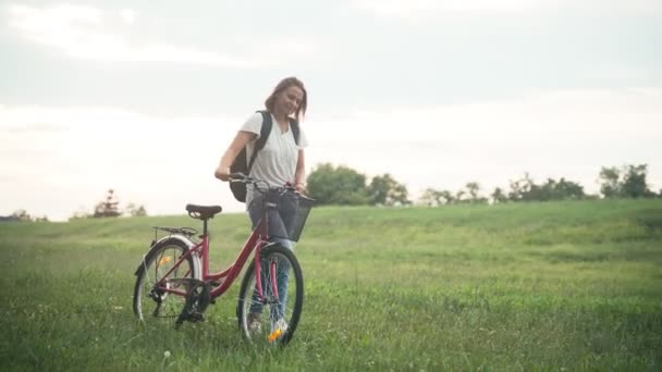 Zdjęcia młodej kobiety spacerującej na zielonym polu z rowerem — Wideo stockowe