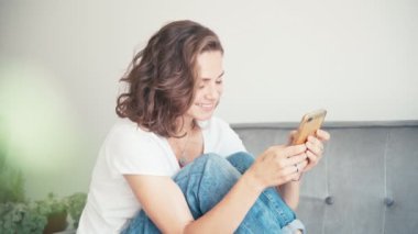Kanepede oturan genç ve güzel bir kadın. Elinde akıllı bir telefonla..