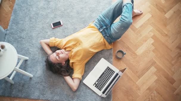 Top view shot of a young woman lying on the floor next to her laptop — Stock Video