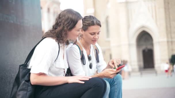 Deux jeunes femmes gaies assises sur un monument dans un centre-ville — Video