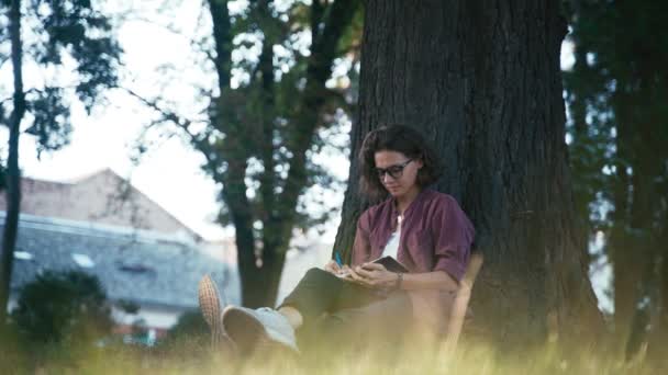 Genç bir kız parkta otururken defterine notlar alır. — Stok video