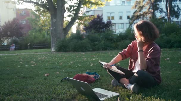 Ung student flicka gör anteckningar i sin anteckningsbok och tar ett telefonsamtal — Stockvideo