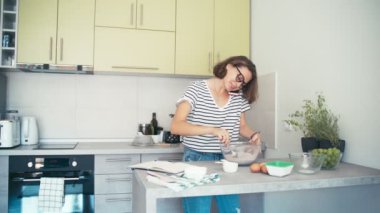 Genç ve neşeli bir kadın telefonuyla konuşurken kaseye malzemeleri karıştırıyor..