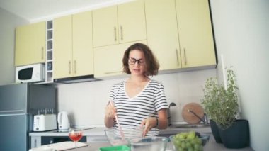 Mutfakta dans eden gözlüklü neşeli genç bir kadın.