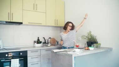 Mutfakta dans eden gözlüklü neşeli genç bir kadın.