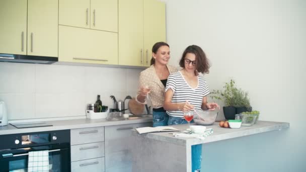 Dos mujeres guapas jóvenes cantando y bailando mientras cocinan en la cocina luminosa — Vídeos de Stock