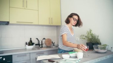 Genç ve neşeli bir kadın yemek yaparken bir bardaktan şarap içer.