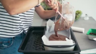 Çikolata hamurunu kaseden pişirme kabına aktarmak için spatula kullanan bir kadın.