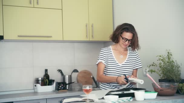 Una mujer joven coloca una hoja de papel para hornear en el fondo de un plato para hornear. — Vídeos de Stock