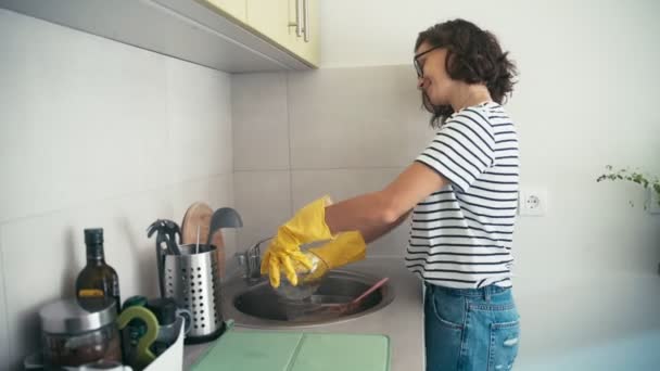 Sarı lastik eldivenli neşeli bir kadının elde çekilmiş fotoğrafı bulaşıkları yıkıyor. — Stok video