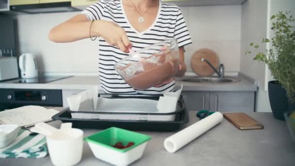 Mujer usando una espátula para transferir masa de chocolate de un tazón a un plato para hornear — Vídeo de stock