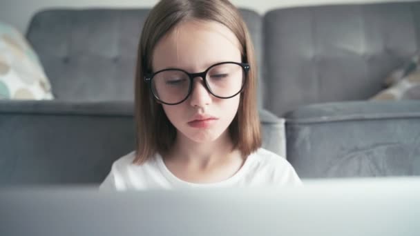 Ernstes kleines 8-jähriges Mädchen mit Brille blickt auf einen Laptop-Bildschirm und tippt — Stockvideo