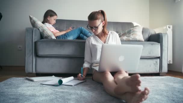 Mujer joven trabajando desde casa, mientras su hija acostada en un sofá — Vídeos de Stock